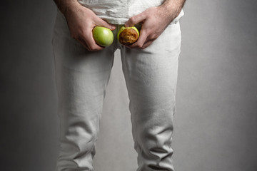 A man at the level of the genitals , holding a ripe and rotten apple. Male suffering with pain in...