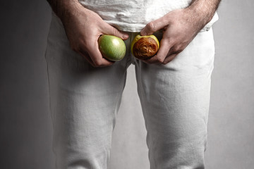A man at the level of the genitals , holding a ripe and rotten apple. Male suffering with pain in...