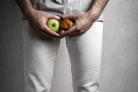 A man at the level of the genitals , holding a ripe and rotten apple. Male suffering with pain in the urogenital system. The concept of protection of sexually transmitted infections. Close up