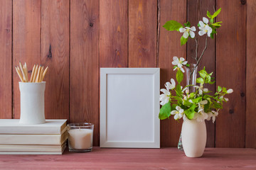 Home interior with decor elements. White frame, white spring flowers in a vase, books, interior decoration