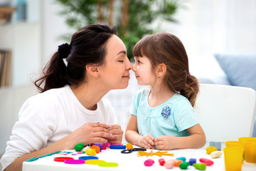 Fototapeta premium Mother's tenderness and love. Mom gently kisses her daughter in the nose. Woman and little girl mold from plasticine