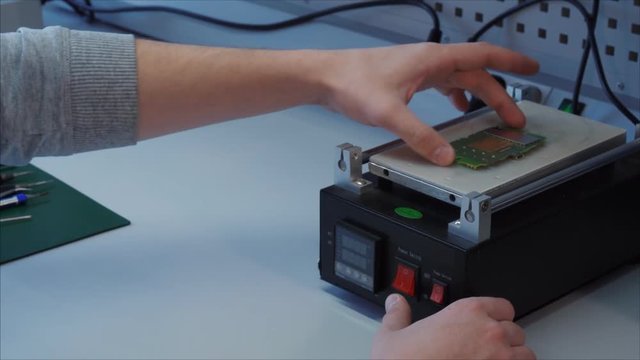 Closeup. A technician repair engineer heats the motherboard from a segway hoover. Presses buttons, setting necessary parameters.