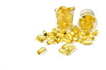 Close up of Golden fish oil capsules isolated in measuring cup on white background. Omega 3 from salmon fish. Vitamin E. Supplementary food. Two glass jar.