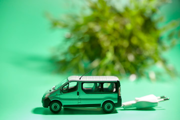 miniature of a vehicle with electric plug next to a plant on a green background