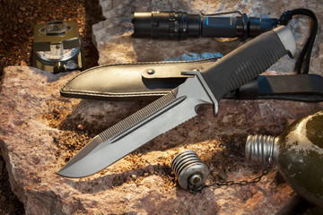 combat knife, scabbard, compass, flashlight and flask on the stone