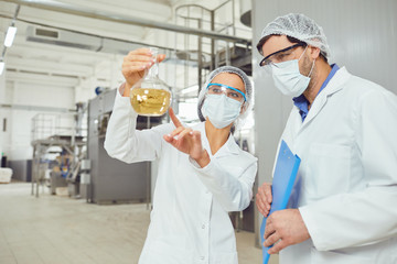 Workers in masks and coats look at the liquid in the flask at work