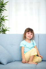 Cute little girl in home clothes sitting in the room on the couch