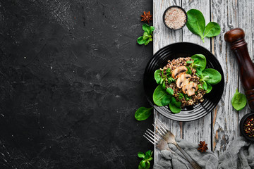 Quinoa with spinach and mushrooms. In a black plate on a wooden background Top view. Free space for your text. Flat lay