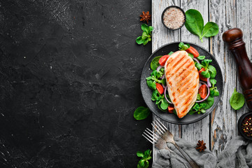Baked chicken fillet with vegetables. In a black plate on a wooden background Top view. Free space for your text. Flat lay - obrazy, fototapety, plakaty