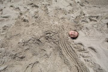 little girl buried in the sand on the beach