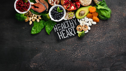 Healthy food for the heart: Fish, blueberries, nuts, pomegranate, avocados, tomatoes, spinach, flax. On a dark background. Top view. Free space for your text.