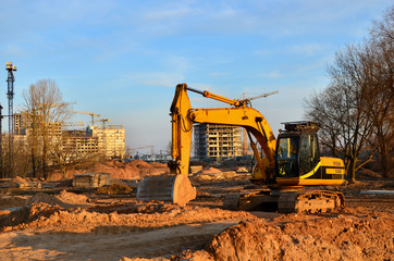 Tracked excavator with a bucket in the ground at a construction site against a blue sky and sunset