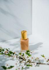 Obraz na płótnie Canvas Foundation cream in golden bottle and branch of blossom cherry tree.