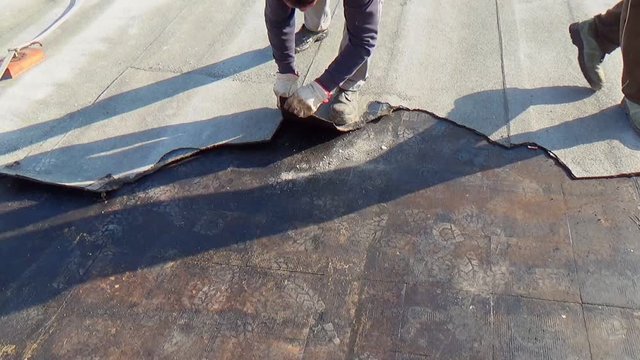 Workers remove the damaged bituminous layer from the flat roof of a building