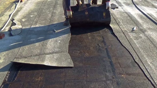 Workers remove the damaged bituminous layer from the flat roof of a building