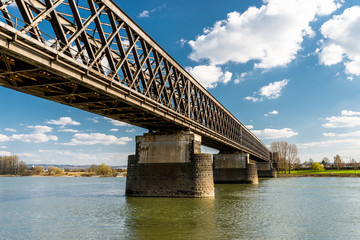 Fototapeta na wymiar Steel, lattice structure of a railway bridge over a river with a background of blue sky with white clouds in western Germany.