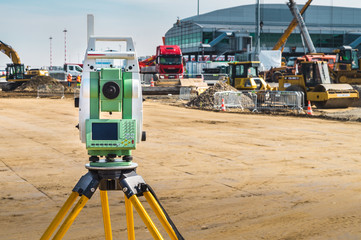 Surveyor engineer with equipment (theodolite or total positioning station) on the construction site of the road or building with construction machinery background