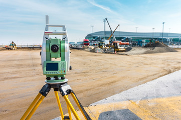 Surveyor engineer with equipment (theodolite or total positioning station) on the construction site of the road or building with construction machinery background