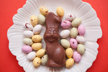 Easter chocolate bunny with eggs on a white plate on a coral background.