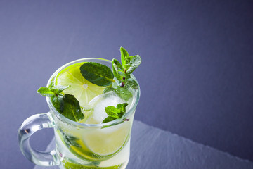 Mojito on black background. Mojito cocktail with lime and fresh mint on slate board. Summer refreshing cocktail with citrus on dark background. Copy space