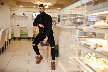 Arab man wear on black jeans jacket and eyeglasses in cafe drink coffee at bar with book. Stylish and fashionable arabian model guy.