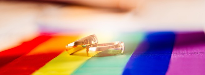Two gold wedding rings on rainbow lgbt flag. Homosexual marriage.
