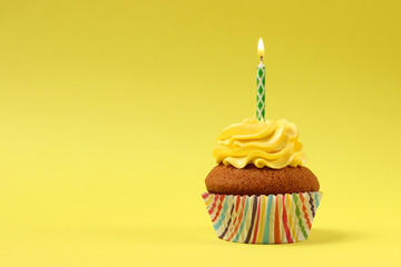  Delicious cupcake with a candle on a colored background with space to insert text. Festive background, birthday.