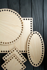 Light wooden parts with holes for making handmade knitted bags on a black surface. Selective soft focus.