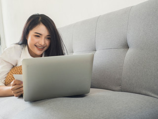 Beautiful woman in a white dress, playing a laptop computer on the sofa. Business ideas and online shopping
