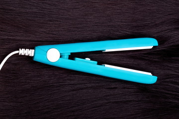hair curling iron on background of black long and straight hair