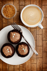 Chocolate fairy cakes, a fork and a cup of coffee on a wooden background