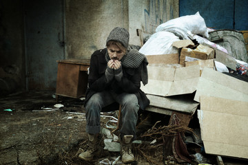 Poor homeless man sitting near rubbish at dump