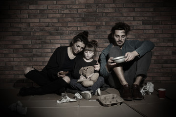Poor family sitting on floor near brick wall