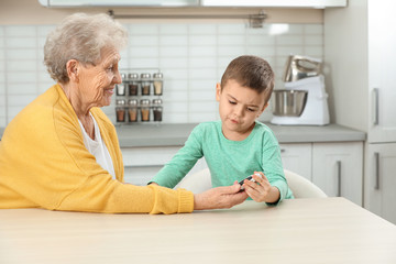 Fototapeta premium Senior woman with her grandson using digital glucometer at home. Diabetes control