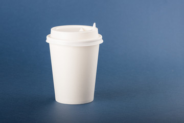 White disposable paper cup with white cap on a blue background