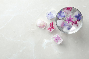 Glass of water and ice cubes with flowers on table, top view. Space for text