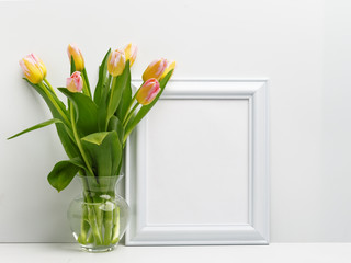 Wooden frame on the table with a bouquet of delicate pink tulips in a glass vase. Copy space.
