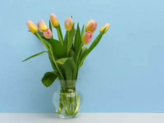 Wooden frame on the table with a bouquet of delicate pink tulips in a glass vase. Copy space.