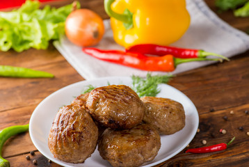 cutlets on a white plate on the background of vegetables and greens. Wooden table and home view