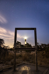 Starry night sky with a lighthouse beacon shining. Wooden frame for tourists positioned in front of the lighthouse. Fire Island New York