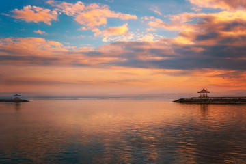 Fototapeta na wymiar Bali Sanur at sunrise on the beach. Beautiful calm water with 2 temples on a breakwater. Great reflection in the water with backlighting and great clouds