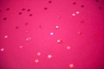 red sparkling sequins stars on red background. Top view, flat lay. Copyspace for text. Bright and festive holiday background.
