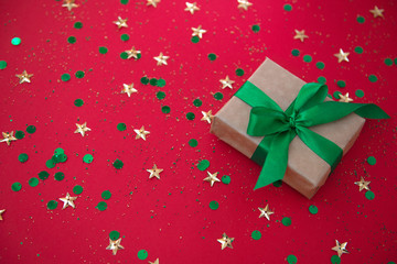 Fototapeta na wymiar gift box on golden sequins and stars red background. Top view, flat lay. Copyspace for text. Festive holiday background.