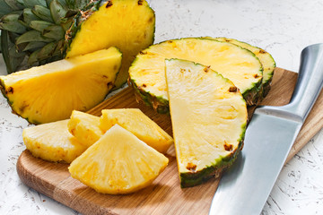 Sliced pineapple on a wooden board on a white background. Pineapple pieces of various sizes