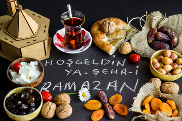Symbolic foods of Ramadan around handwriting  Welcome Ramadan by Turkish letters on the black background.Wooden model mosque near foods.