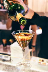 Barman pouring fresh alcoholic drink from bottle into an elegant martini glass on the bar counter