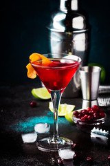 Classic alcoholic cocktail cosmopolitan with vodka, liqueur, cranberry juice, lime, ice and orange zest, dark bar counter background, night mood, space for text