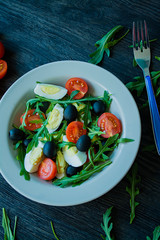 Greek salad with fresh tomatoes, arugula, eggs, olives with olive oil on a dark wood background. Healthy food. Veggie dish.