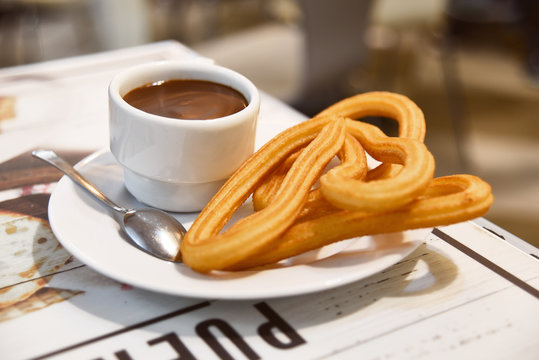 Traditional Spanish dessert churos with hot spicy chocolate and sugar in a pan on a wooden table, selective focus