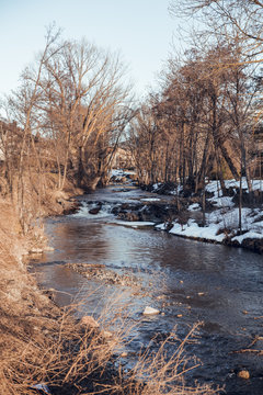 Narrow river running between dry trees and snow in Cerdanya, France